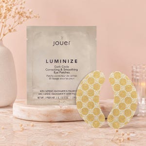 May include: A package of Jouer Luminize Dark Circle Correcting & Smoothing Eye Patches. The package is white with black text. Two gold-colored eye patches with a geometric pattern are next to the package. The net weight is 5.6 g / 0.17 oz.