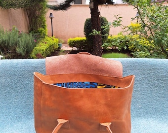 Puede incluir: Un bolso tote de cuero marrón con un forro de tela estampado en azul y amarillo. El bolso tiene dos asas y está abierto, revelando el forro.