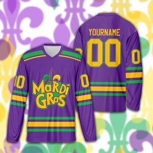 May include: Purple long-sleeved jersey with green and yellow accents. The front features the text "Mardi Gras" in yellow and green, along with a fleur-de-lis. The back displays "YOURNAME" above the number "00" in yellow.