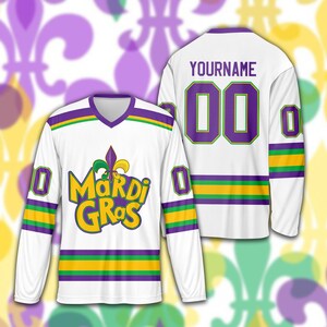 May include: White long-sleeved hockey jersey with purple, green, and yellow accents. The front features the words "Mardi Gras" in yellow and green, with a fleur-de-lis. The back has the name "YOURNAME" and the number "00".
