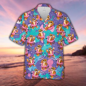 May include: A short-sleeve button-down shirt featuring a repeating pattern of cartoon tigers wearing sunglasses and holding drinks while inside pink flamingo pool floats, set against a purple background with teal geometric shapes and patterns.