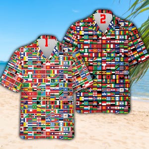 May include: Two short-sleeved button-down shirts with a vibrant pattern of international flags. One shirt has a red number "2" on the back. The shirts are on a sandy beach with a blue sky and palm tree in the background.