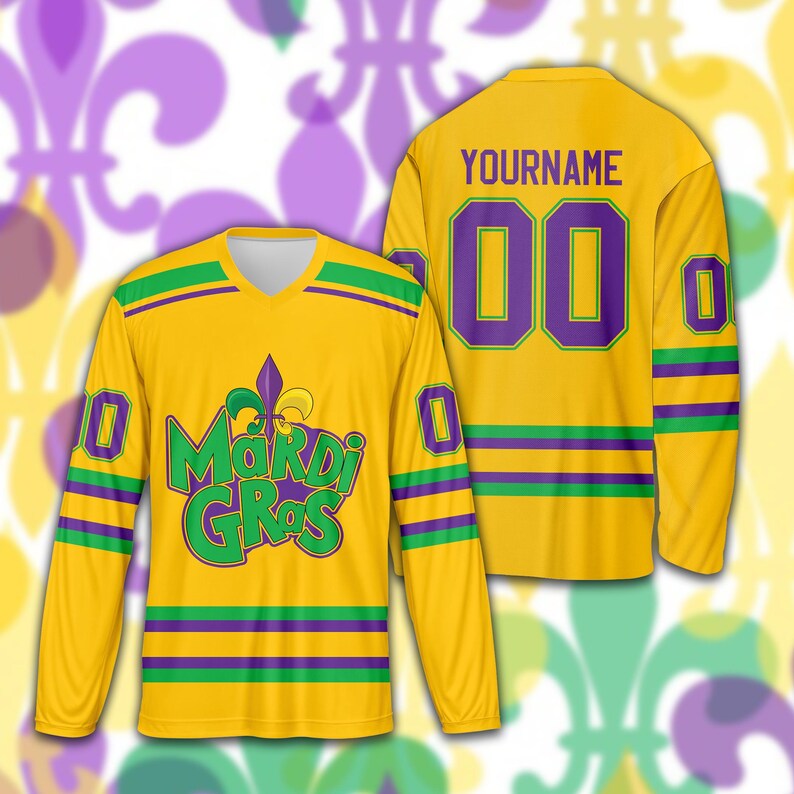 May include: A yellow long-sleeved jersey with green and purple stripes and accents. The front features the text "Mardi Gras" in green and a purple fleur-de-lis. The back displays the number "00" in purple and the name "YOURNAME".