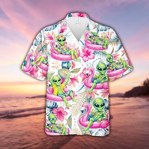 May include: White Hawaiian shirt featuring a repeating pattern of green aliens relaxing on pink flamingo floats, holding drinks. The shirt is decorated with tropical flowers and foliage. The background shows a beach scene.