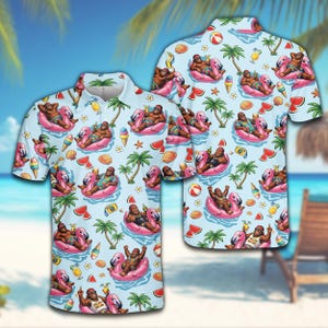 May include: Light blue short-sleeved polo shirt with a repeating pattern of a cartoon character on a flamingo float, palm trees, watermelon slices, and ice cream cones. The shirt has a button-down collar.