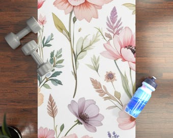 May include: A white yoga mat with a watercolor floral design featuring large pink and purple flowers, green leaves, and stems. Gray dumbbells and a blue water bottle are visible.