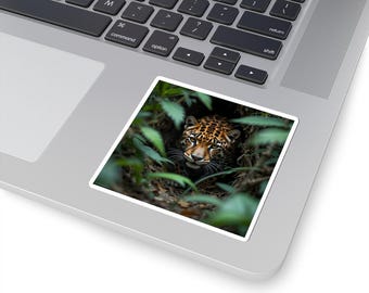 May include: A square sticker featuring a close-up of a jaguar's face peering out from lush green foliage. The jaguar has a spotted coat and is partially hidden among the leaves, creating a sense of depth and mystery.