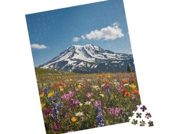 Può includere: Puzzle completato raffigurante un paesaggio montano con una vetta innevata sotto un cielo blu nuvoloso. Il primo piano mostra un campo vibrante di fiori selvatici.