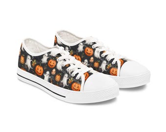 May include: Pair of Halloween-themed canvas sneakers. The black canvas is patterned with orange jack-o'-lanterns and white ghosts. The shoes have white laces, a white toe cap, and a black stripe along the white sole.