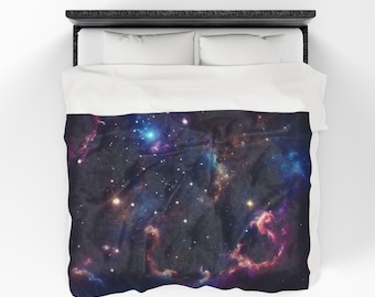 Puede incluir: Una funda nórdica azul oscuro con un estampado de galaxia que presenta una nebulosa con tonos rosados, azules y morados y una dispersión de estrellas.