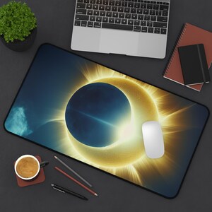 Puede incluir: Una alfombrilla de ratón negra y azul con un diseño de eclipse solar amarillo y naranja.