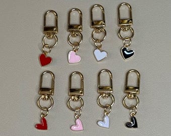 Pode incluir: Oito chaveiros de ouro com pingentes em forma de coração. Os pingentes são vermelhos, rosa, brancos e pretos.