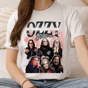 Puede incluir: Camiseta blanca con un dise&ntilde;o de Ozzy Osbourne. El dise&ntilde;o presenta el texto "OZZY Osbourne" en una fuente estilizada, junto con m&uacute;ltiples im&aacute;genes del m&uacute;sico sobre un fondo rosa y blanco.