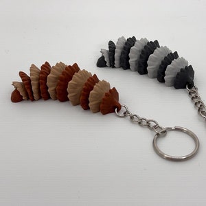 May include: Two keychains with a silver chain and a ring. One keychain has a series of brown, tan, and orange fan-shaped charms. The other keychain has a series of gray, black, and white fan-shaped charms.