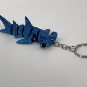 May include: A blue hammerhead shark keychain with a silver metal key ring.