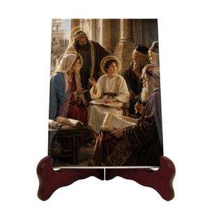 Puede incluir: Una baldosa de cerámica con una pintura religiosa de una persona joven con túnica blanca, rodeada de varias personas mayores. La baldosa se exhibe en un caballete de madera rojo oscuro. La pintura representa una escena con figuras con túnicas y halos.