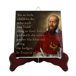 May include: A square decorative tile featuring a portrait of a bearded man in red clerical robes with a small cross necklace. The text reads: Do as little children do, who with one hand cling to their father, and with the other gather blackberries along the hedges. St Francis of Sales.