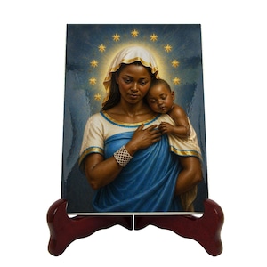 Può includere: Una stampa d'arte religiosa raffigurante una donna con un velo bianco e una veste blu che tiene in braccio un bambino. L'immagine presenta un'aureola di stelle dorate attorno alla testa della donna. La stampa è esposta su un supporto in legno rosso scuro.