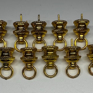 May include: A set of ten gold-colored metal furniture pulls, each featuring a tiered, decorative top section with a textured rope-like band and a small, circular ring handle hanging from the base, topped with a short, straight mounting pin.
