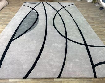 Puede incluir: Una alfombra rectangular grande de color gris claro. Líneas y formas negras y curvas en negrita crean un diseño abstracto en la superficie. La alfombra está hecha de un material suave y texturizado, adecuado para una sala de estar o un dormitorio. Las dimensiones de la alfombra son en centímetros.