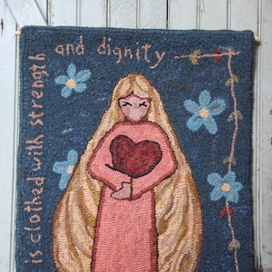 May include: A needlepoint wall hanging with a blue background and a woman holding a red heart. The text "She is clothed with strength and dignity" and "Proverbs 31:25" are included in the design.