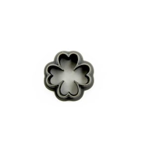 May include: A gray plastic four-leaf clover cookie cutter. The cutter has a rounded shape with four distinct heart-shaped leaves. The object is set against a white background.