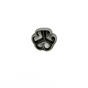 May include: A dark gray, three-leaf clover-shaped cookie cutter. The cutter is made of plastic and has a smooth, rounded edge. The clover shape is divided into three distinct sections.