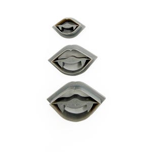 May include: Three gray plastic cookie cutters in the shape of vampire fangs. The cutters are arranged vertically, with the smallest at the top and the largest at the bottom. The cutters are on a white background.