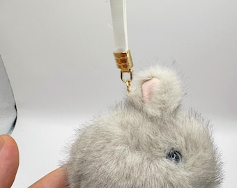 May include: A fluffy gray bunny keychain with pink ears and a white leather strap attached to a gold key ring.