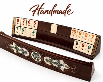 Könnte beinhalten: Ein Okey-Spielständer-Set aus dunklem Holz mit Perlmutt-Intarsien und Messingakzenten. Die Ständer tragen das Wort HELENA an den Seiten. Ein Ständer hält cremefarbene Spielsteine mit roten, grünen und orangefarbenen Zahlen und Herzsymbolen.