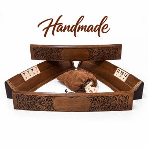 Könnte beinhalten: Ein Set aus vier geschwungenen Holzständern für ein Fliesenspiel aus dunkelbraunem Holz mit filigranen, lasergravierten Blumenmustern. Das Set enthält einen braunen Wildlederbeutel mit Spielsteinen, wobei die Zahlen 7, 11, 12 und 13 auf den Ständern zu sehen sind. Das Wort Handmade steht in brauner Schrift darüber.
