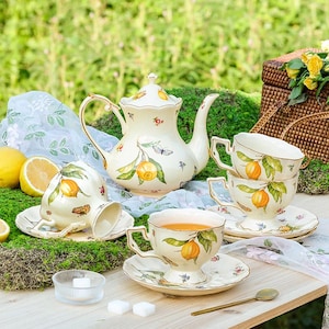 May include: A porcelain tea set featuring a lemon design. The set comprises a teapot, four teacups, and four saucers. The teacups and saucers are adorned with a lemon tree branch and lemons. The teapot has a floral pattern and a lemon tree branch with lemons on the side.