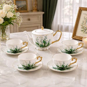 Könnte beinhalten: Ein weißes Porzellan-Teeservice mit goldenen Akzenten, bestehend aus einer Teekanne, vier Tassen und Untertassen. Jedes Teil ist mit einem grünen und blauen Blumenmuster verziert. Das Set steht auf einer Marmoroberfläche.