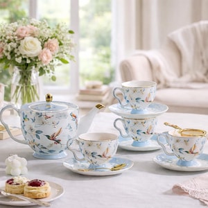 Può includere: Servizio da tè in porcellana con un motivo di colibrì e floreale. Il set include una teiera, tazze, piattini e un colino da tè. Le tazze e i piattini hanno una base azzurra e bordi dorati.