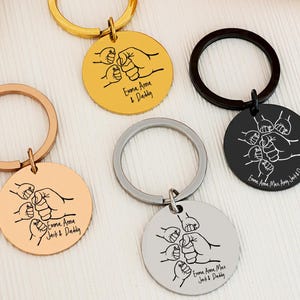 May include: Five metal keychains in gold, rose gold, silver, and black. Each keychain features a round pendant with a drawing of hands and the text "Emma Anna, Max & Daddy" or "Jack & Daddy".