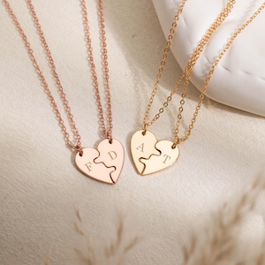 Könnte beinhalten: Zwei Sets aus passenden herzförmigen Anhängerketten an dünnen Ketten. Ein Set ist in Roségold gehalten und mit den Buchstaben F und D auf den Herzhälften graviert. Das andere Set ist in Gelbgold mit den Buchstaben A und T auf den Herzhälften.