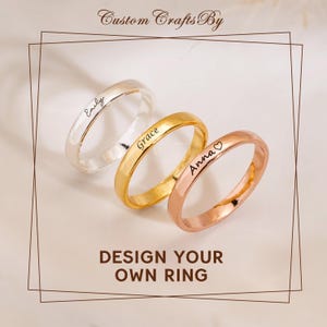 May include: Three personalized rings in silver, gold, and rose gold. Each ring is engraved with a name: "Emily", "Grace", and "Anna". The rings are displayed on a light background with the text "DESIGN YOUR OWN RING".