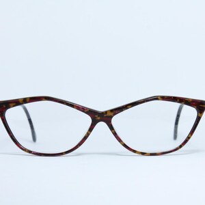 Può includere: Un paio di occhiali con montatura a fantasia tartarugata. Le montature a occhi di gatto presentano un motivo rosso scuro e giallo. Le lenti sono trasparenti e le aste sono nere.