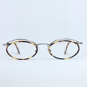 Könnte beinhalten: Ovale Brille mit Schildpattmuster an den Rändern und Bügeln. Die Fassung kombiniert silberfarbenes Metall mit dem Schildpatt-Design. Die Gläser sind klar, vor weißem Hintergrund.