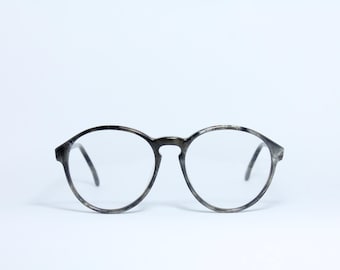 May include: Round eyeglasses with a speckled gray and black frame. The lenses are clear, and the temples are thin and dark. The glasses are set against a white background.