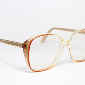 Könnte beinhalten: Vintage Brille mit transparentem Rahmen und braunen Bügeln. Die Gläser sind klar, und die Rahmen haben eine rechteckige Form mit einem braunen Akzent an den Rändern. Ein klassisches Brillenaccessoire.