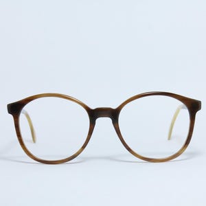 May include: Round-framed eyeglasses with a brown gradient. The frames transition from a darker brown at the top to a lighter brown towards the bottom. The temples are a light tan color. The lenses are clear.