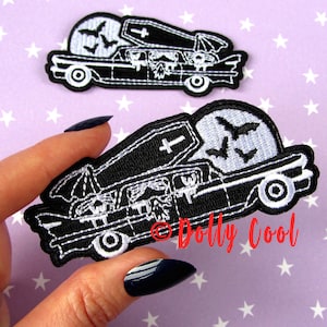 May include: Two black and white embroidered patches. One patch shows a hearse with a coffin on top, bats, and a full moon. The other patch is a close-up of the same design. The patches are on a purple background with white stars.