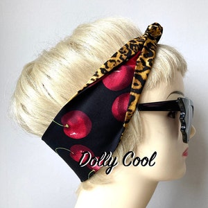 May include: A black and red headband with a cherry and leopard print. The headband is tied in a knot at the top of the head. The text "Dolly Cool" is printed on the headband.