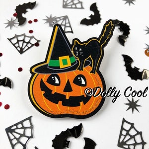 Peut inclure: Une citrouille d'Halloween en bois avec un chat noir portant un chapeau de sorcière sur le dessus. La citrouille a un visage de citrouille sculpté et est peinte en orange. Le chat est noir avec des yeux blancs et un chapeau vert avec une boucle verte. L'arrière-plan est blanc avec des décorations d'Halloween éparpillées.