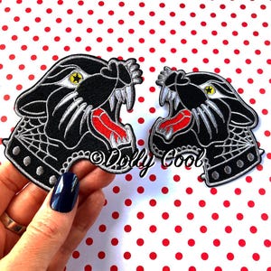May include: Two black panther head iron-on patches with red mouths and white teeth. The patches have a silver outline and a black and white spider web design on the collar.