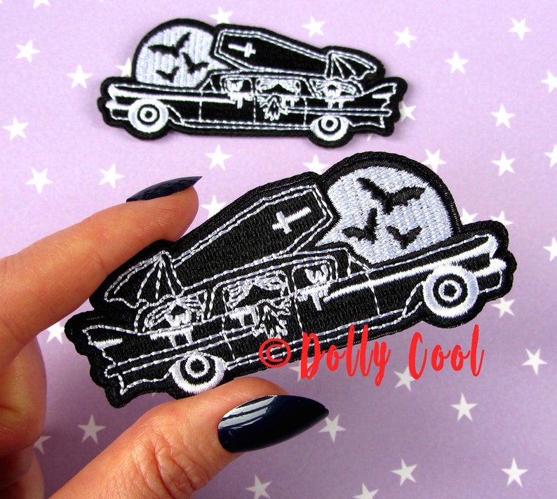 Pu&ograve; includere: Due toppe ricamate in bianco e nero. Una mostra un carro funebre con una bara sopra, pipistrelli e una luna piena. L'altra toppa &egrave; un primo piano dello stesso disegno. Le toppe sono su uno sfondo viola con stelle bianche.