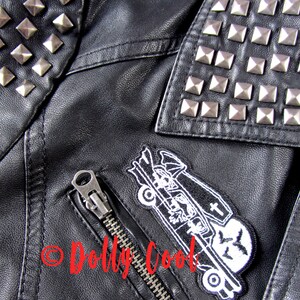 Pu&ograve; includere: Giacca in similpelle nera con borchie piramidali argentate su spalle e colletto. Presenta una tasca frontale con cerniera e una toppa con un design a carro funebre. Stile biker classico.