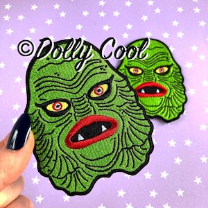 May include: Two green embroidered iron-on patches of the Creature from the Black Lagoon. The patches feature the creature's face with red lips and yellow eyes.
