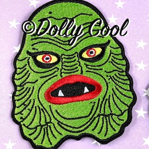May include: Green embroidered patch of the Creature from the Black Lagoon's face with red lips and yellow eyes. The patch has the text "Dolly Cool" in white lettering.